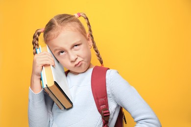 Photo of Funny little girl with backpack and textbooks on yellow background. Space for text