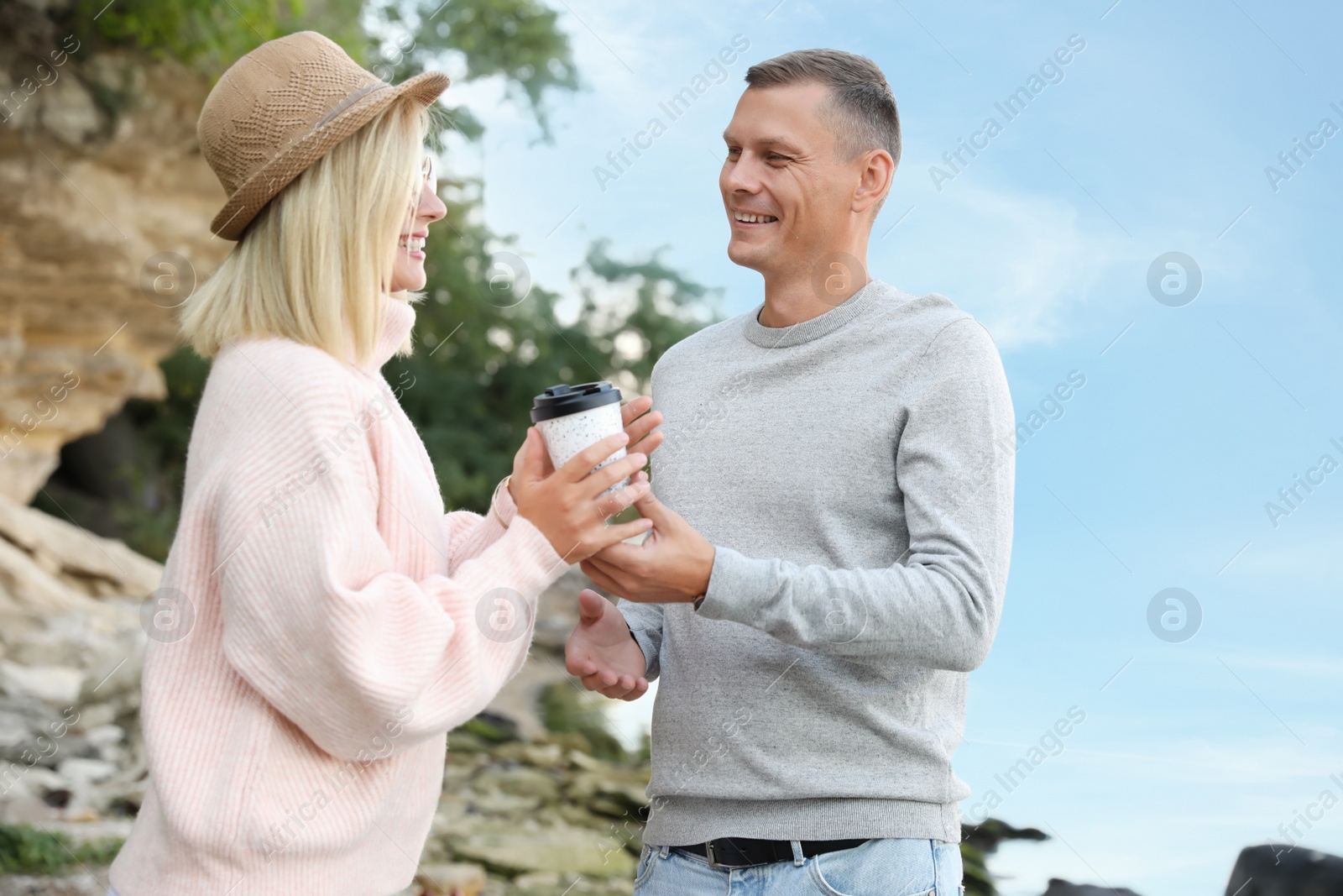Photo of Happy couple in stylish sweater holding drink outdoors