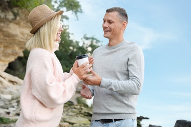 Happy couple in stylish sweater holding drink outdoors