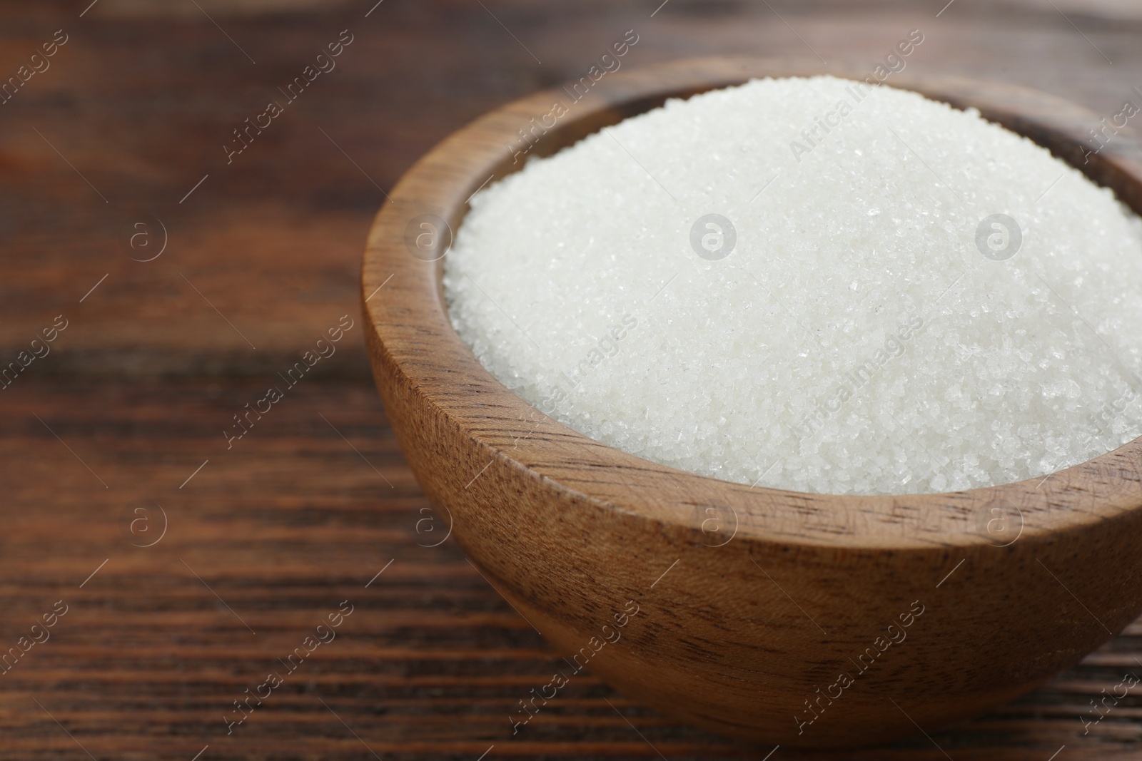 Photo of Granulated sugar in bowl on wooden table, closeup. Space for text