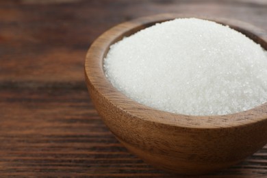 Photo of Granulated sugar in bowl on wooden table, closeup. Space for text