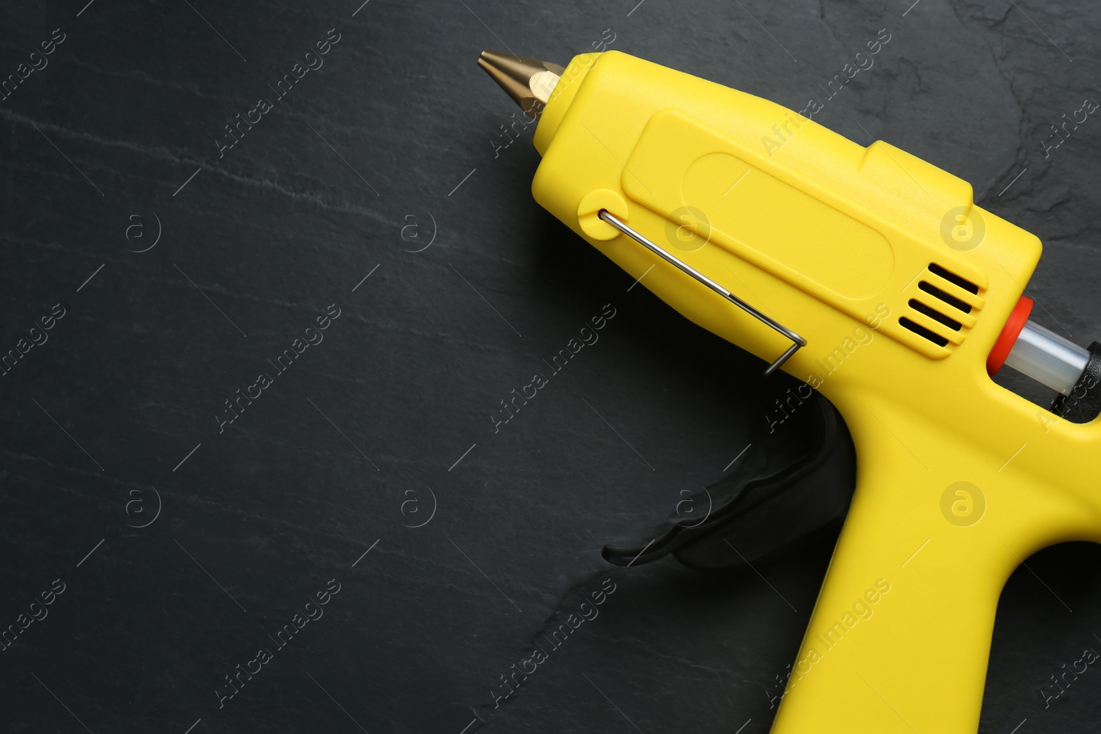 Photo of Yellow glue gun with stick on black table, top view. Space for text