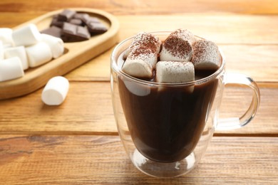 Photo of Cup of aromatic hot chocolate with marshmallows and cocoa powder on wooden table, closeup