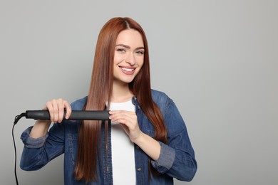 Beautiful woman using hair iron on light gray background, space for text