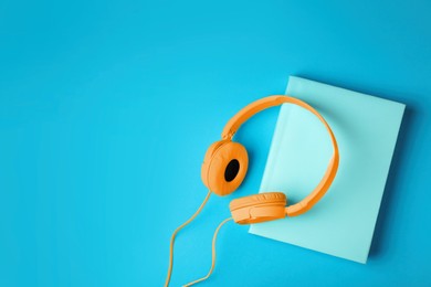 Modern orange headphones with hardcover book on light blue background, top view. Space for text