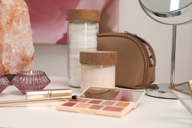 Photo of Cosmetic products, brush, burning candle and mirror on dressing table, closeup