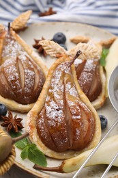 Delicious pears baked in puff pastry with powdered sugar served on table, closeup