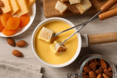 Pot of tasty cheese fondue and snacks on light wooden table, flat lay