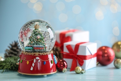 Photo of Beautiful snow globe with Christmas tree, gifts and decor on light blue table
