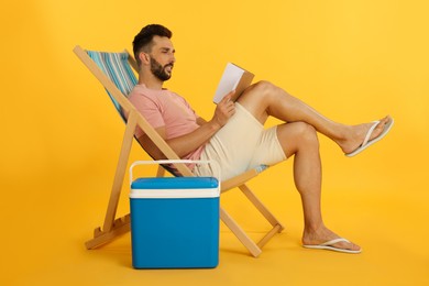 Photo of Man reading book in deck chair near cool box on yellow background