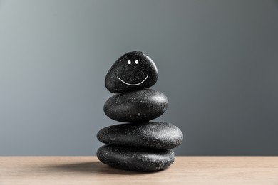 Photo of Stack of stones with drawn happy face on table against grey background. Zen concept