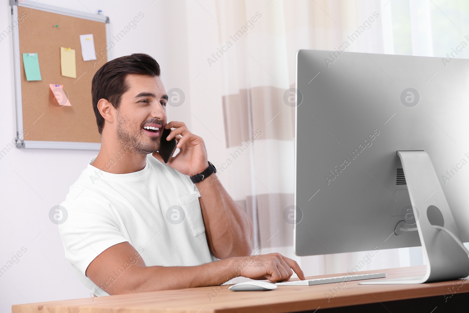 Photo of Handsome young man working with smartphone and computer at table in office