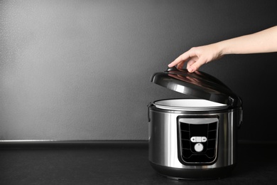 Photo of Young woman using modern multi cooker on table, space for text