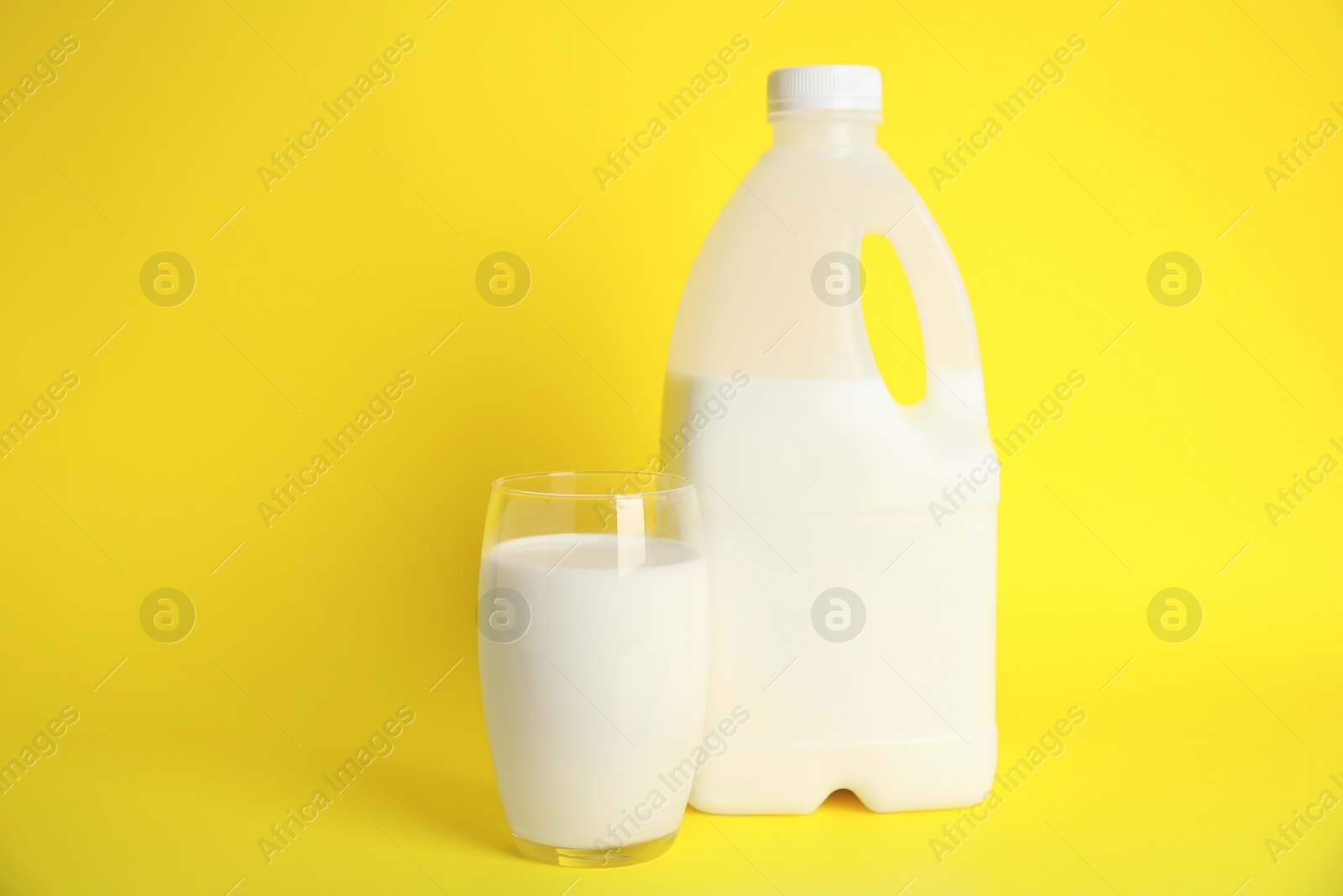Photo of Gallon bottle and glass of milk on yellow background