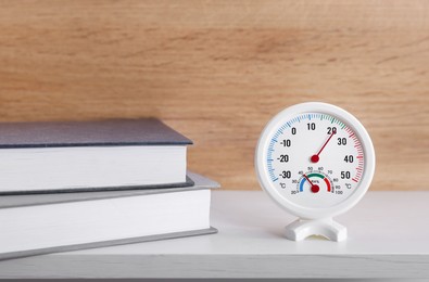 Round hygrometer with thermometer and books on white table