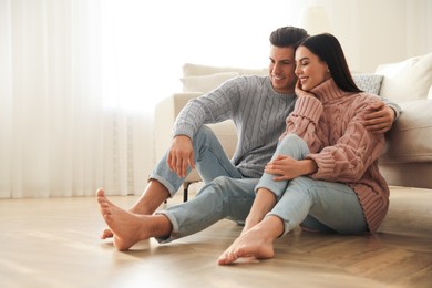 Photo of Happy couple sitting on warm floor in living room. Heating system