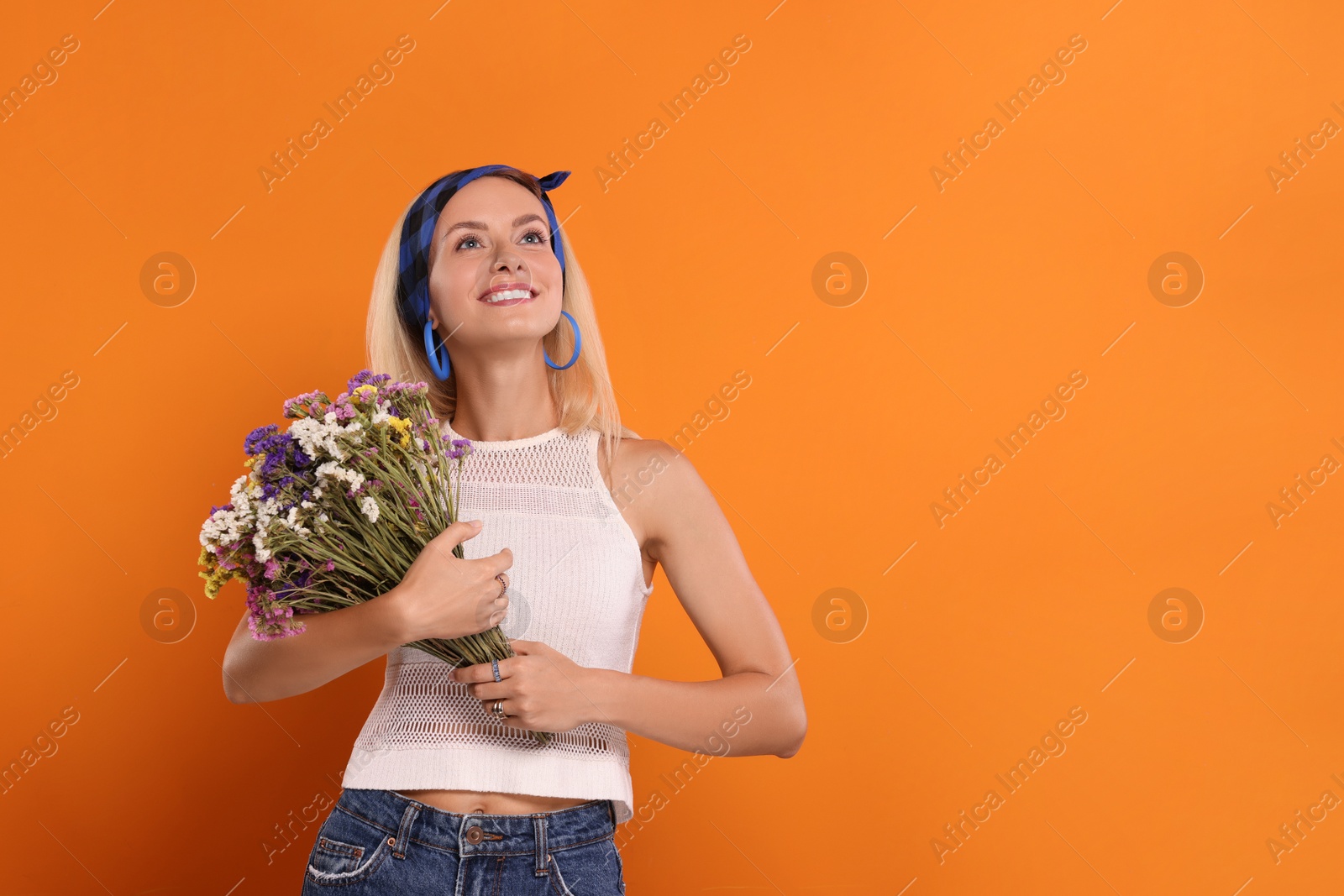 Photo of Happy hippie woman with bouquet of flowers on orange background. Space for text