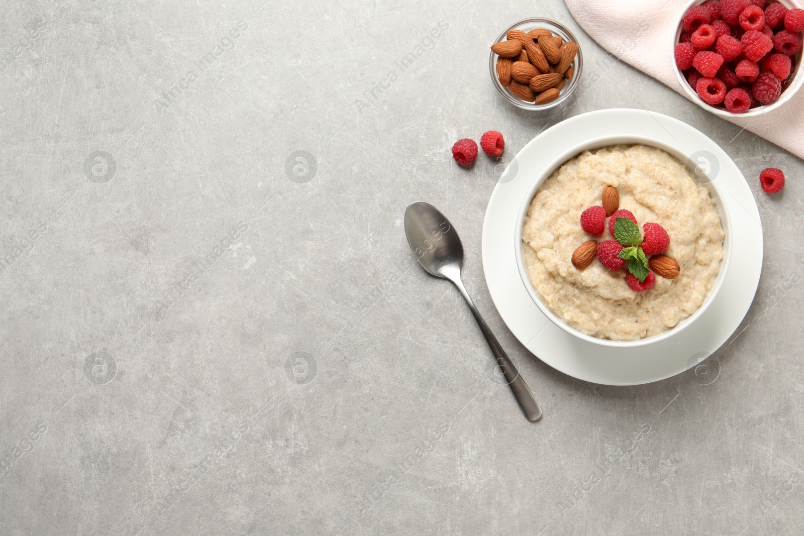 Photo of Tasty oatmeal porridge with raspberries and almond nuts served on light grey table, flat lay. Space for text
