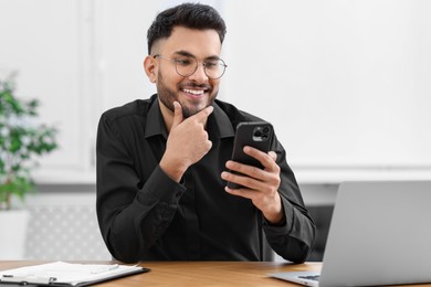 Handsome young man using smartphone at wooden table in office