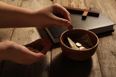 Photo of Donate and give concept. Woman putting coin into bowl with money at wooden table, closeup