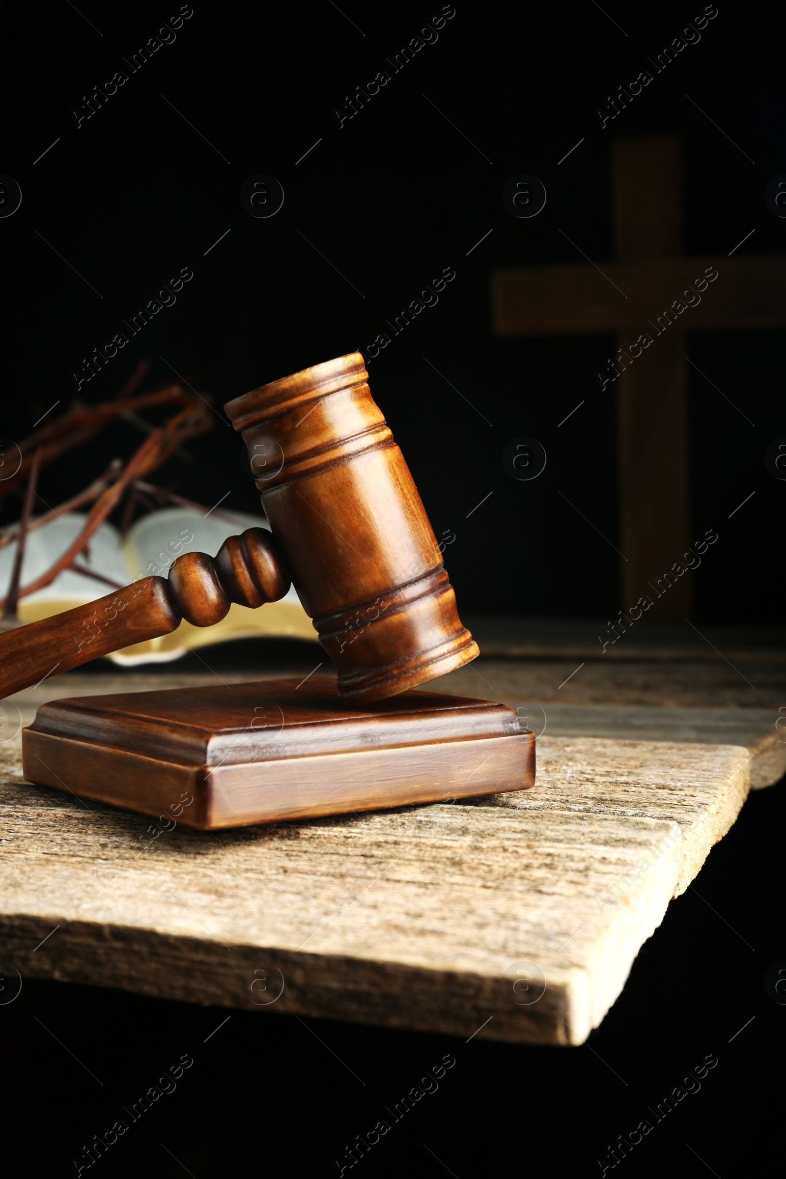 Photo of Judge gavel, bible, cross and crown of thorns on wooden table against black background