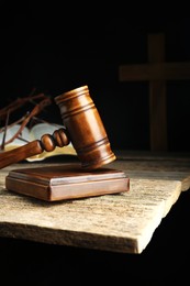 Judge gavel, bible, cross and crown of thorns on wooden table against black background