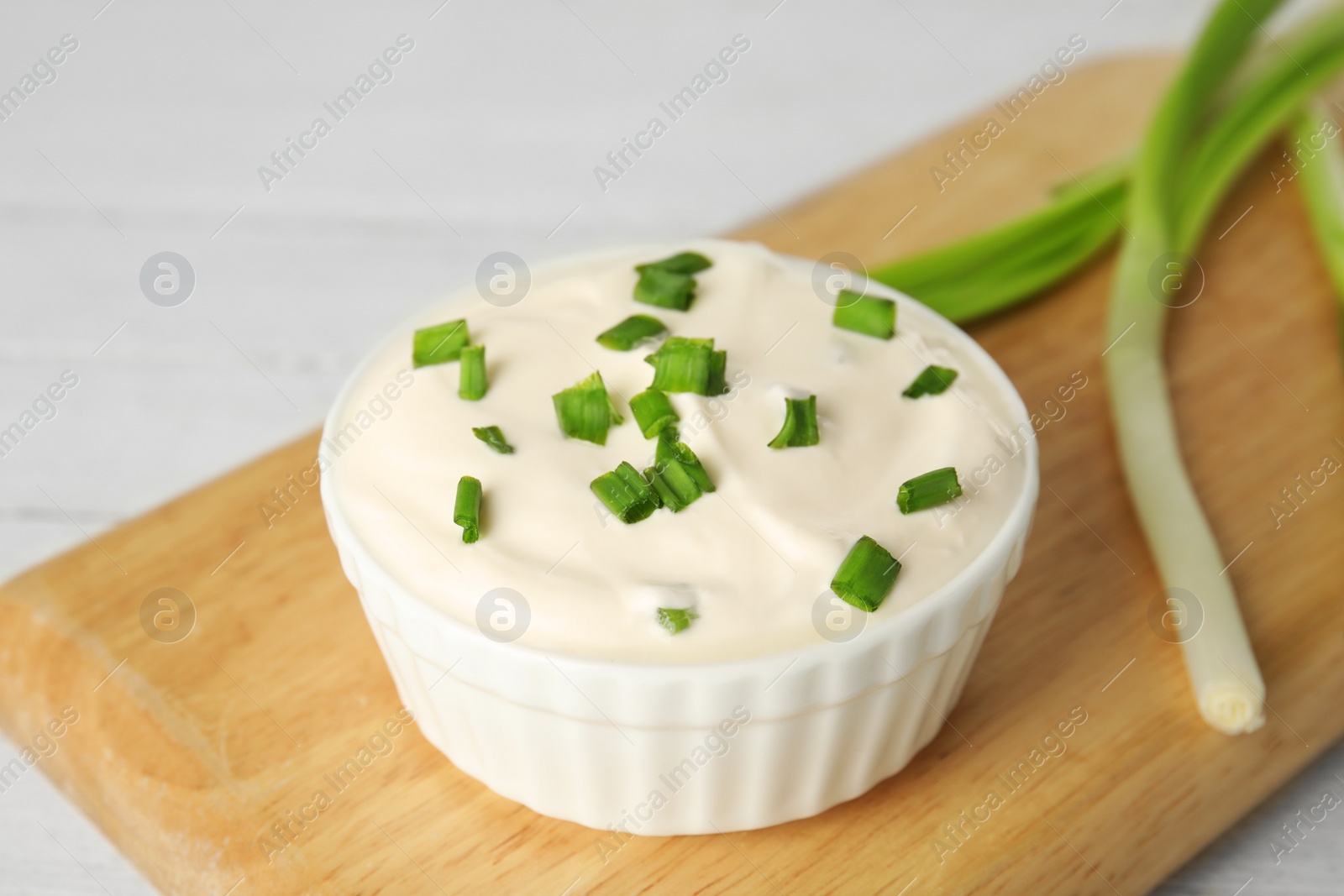 Photo of Fresh sour cream with onion on wooden board, closeup