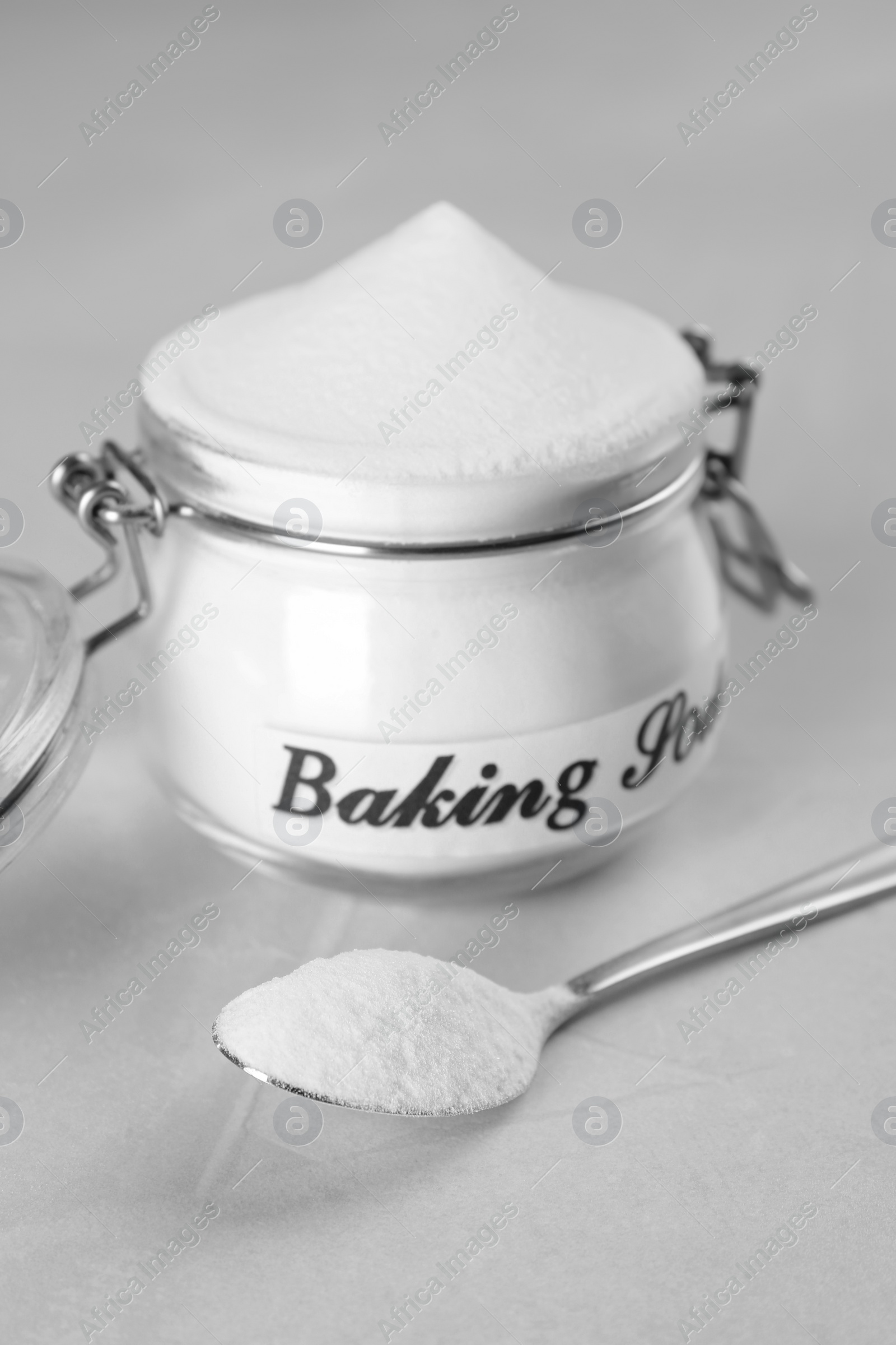 Photo of Spoon and jar with baking soda on light table, closeup