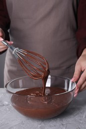 Woman with whisk mixing chocolate cream at table against grey background, closeup