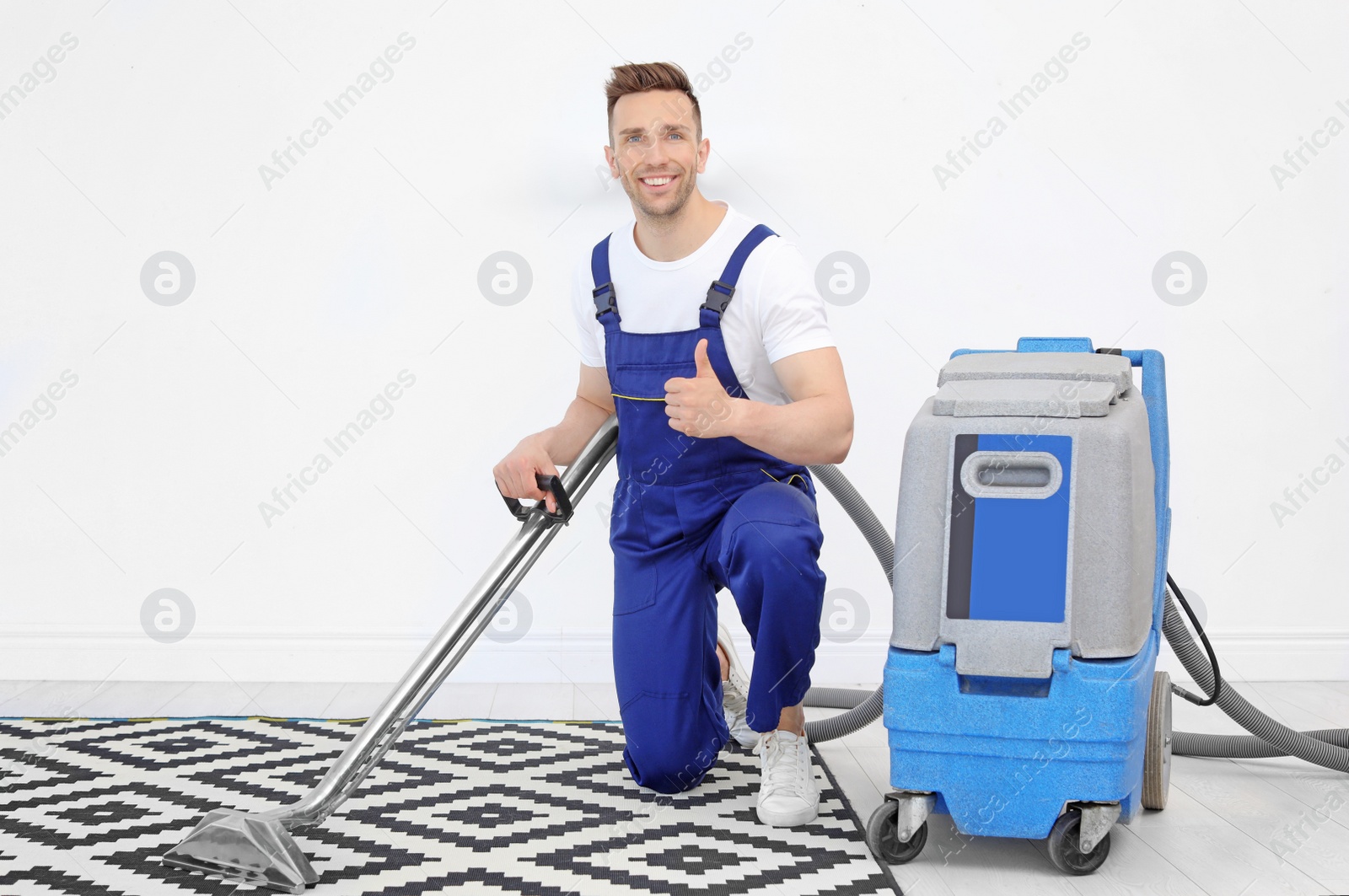 Photo of Male worker removing dirt from carpet with professional vacuum cleaner indoors