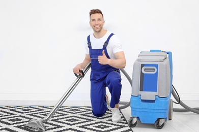 Male worker removing dirt from carpet with professional vacuum cleaner indoors