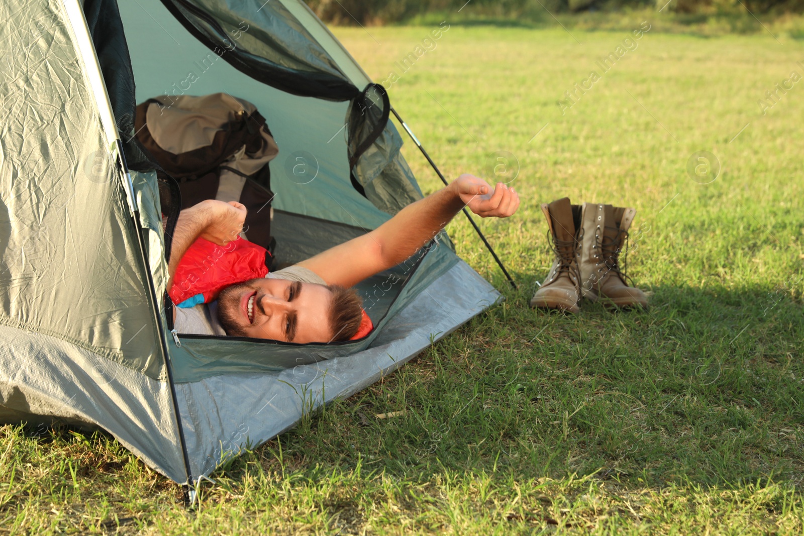 Photo of Happy young man stretching in sleeping bag inside camping tent