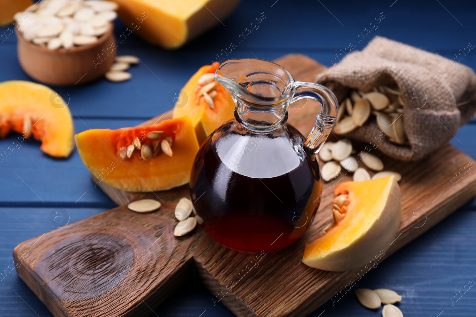 Photo of Fresh pumpkin seed oil in glass jug on blue wooden table