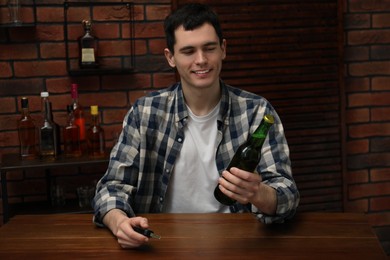 Photo of Smiling man with bottle of beer and car keys at table in bar. Don't drink and drive concept