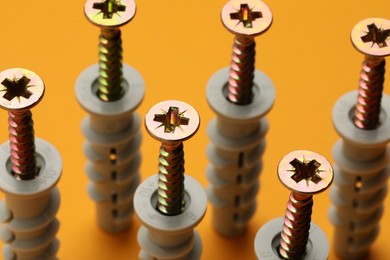 Photo of Many metal screws with dowels on orange background, closeup