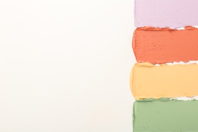 Samples of different color correcting concealers on white background, top view