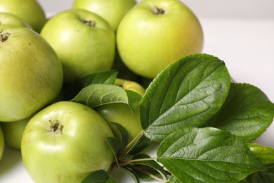 Photo of Fresh ripe green apples with leaves on white table, closeup