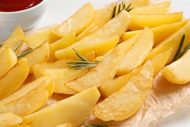 Photo of Tasty baked potato wedges and rosemary on table, closeup