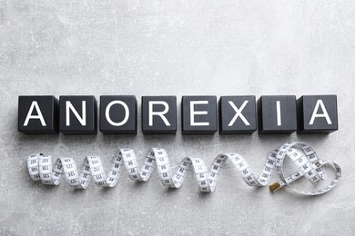 Photo of Word Anorexia made of cubes with letters near measuring tape on light table, flat lay