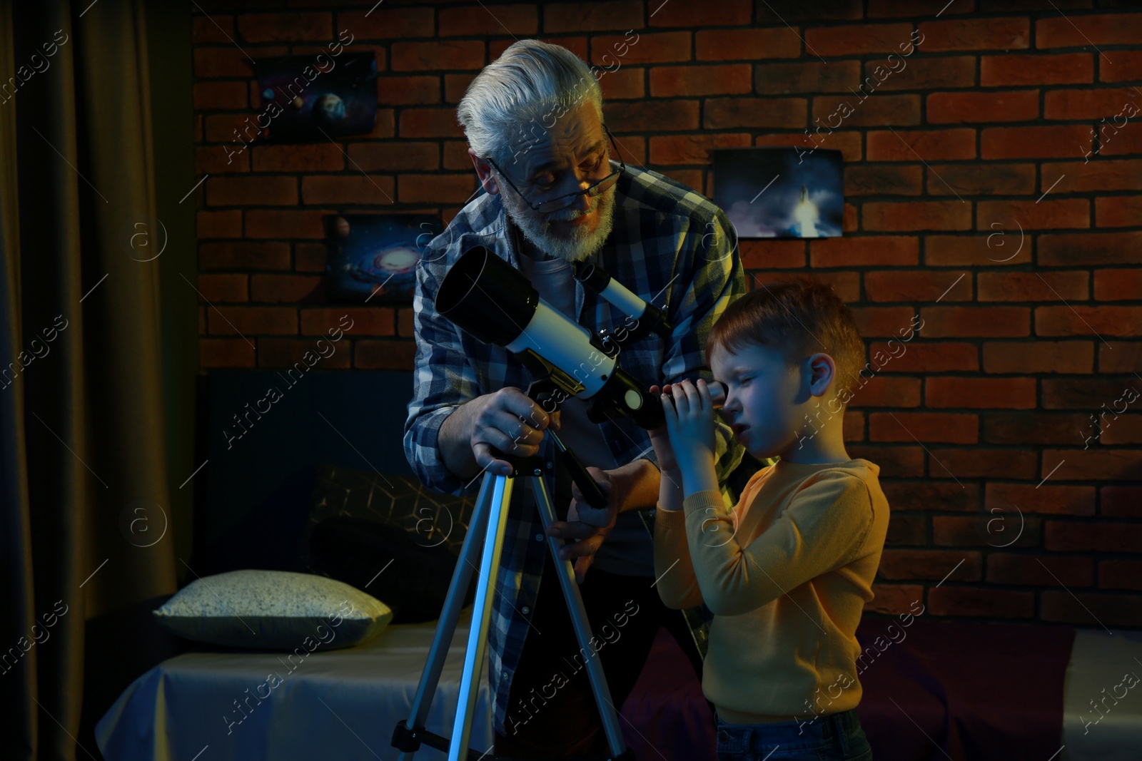 Photo of Little boy with his grandfather looking at stars through telescope in room