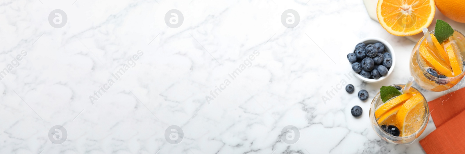 Image of Flat lay composition of delicious orange lemonade with soda water, mint and blueberries on white marble table, space for text. Banner design