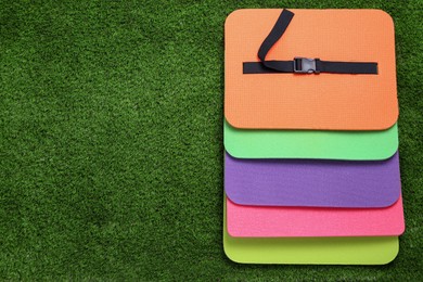 Photo of Bright foam tourist seat mats on green grass, flat lay. Space for text