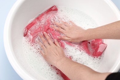 Woman washing baby clothes in basin on light blue background, closeup