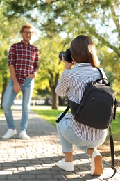 Young female photographer taking photo of man with professional camera in park