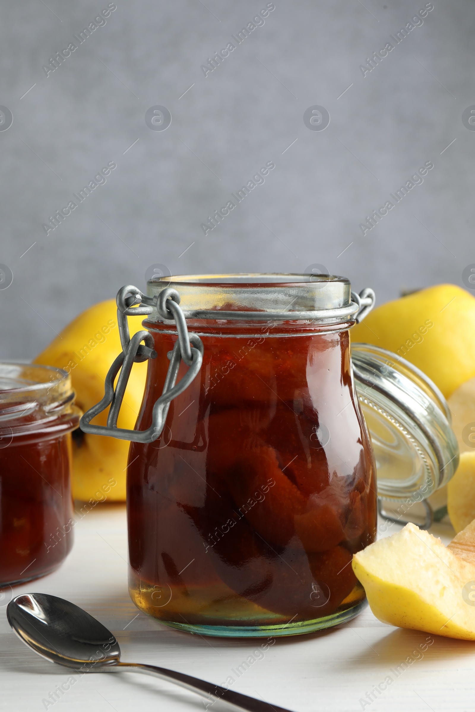 Photo of Tasty homemade quince jam in jar, spoon and fruits on white wooden table, closeup