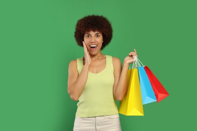 Emotional young woman with shopping bags on green background