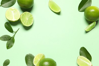 Whole and cut fresh ripe limes with leaves on light green background, flat lay