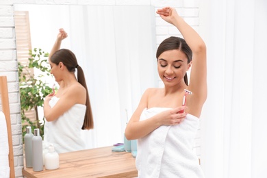 Beautiful young woman shaving armpit at home