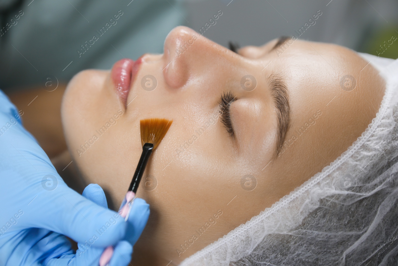 Photo of Cosmetologist applying chemical peel product on client's face in salon, closeup