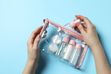 Cosmetic travel kit. Woman putting small bottle with personal care product into plastic bag against light blue background, top view